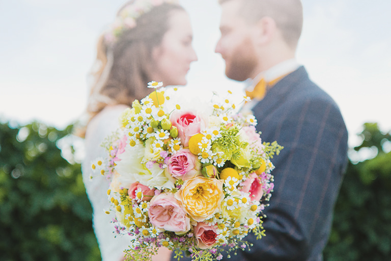 Brautpaar hält vor dem Kuss zusammen einen Blumenstrauß.