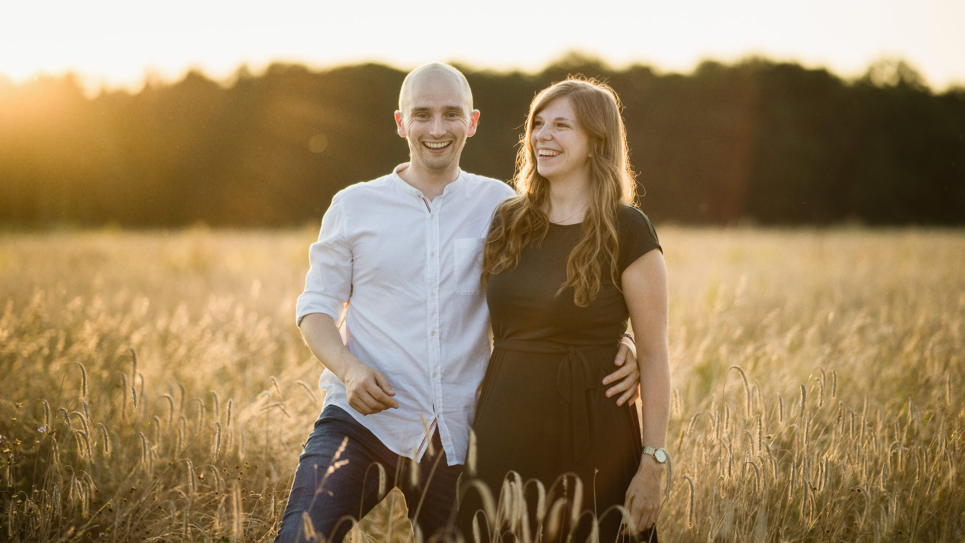 Verlobtes Paar spaziert auf einem Feld beim Sonnenuntergang und freut sich auf die Hochzeit.